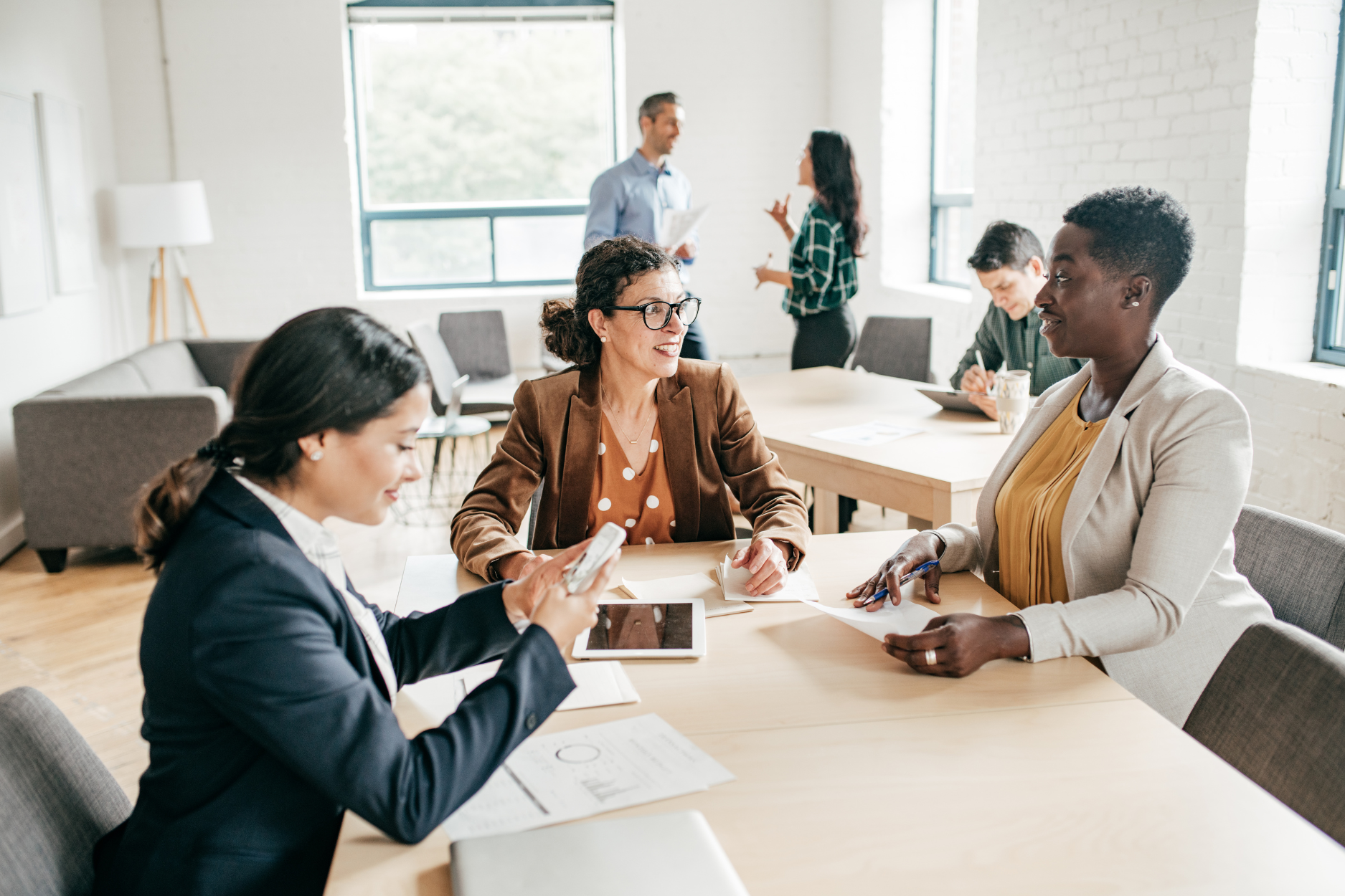 Three business professionals engaged in discussion at a conference table in a modern office setting.