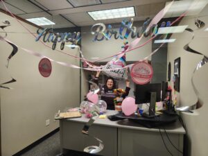 Smiling woman holds happy birthday sign in a decorated office