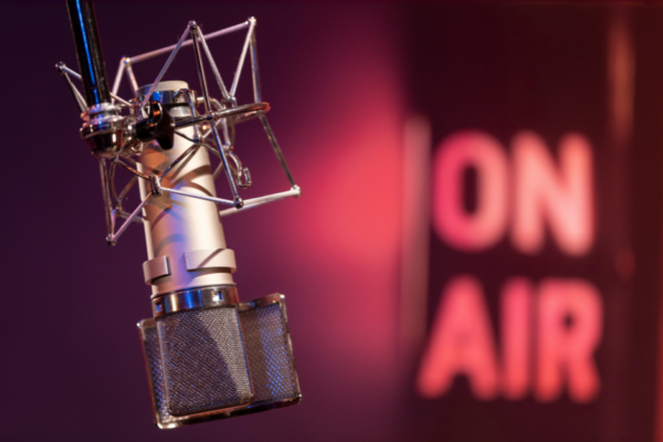 Photo of a professional microphone, with a sign in the background that says "on air"